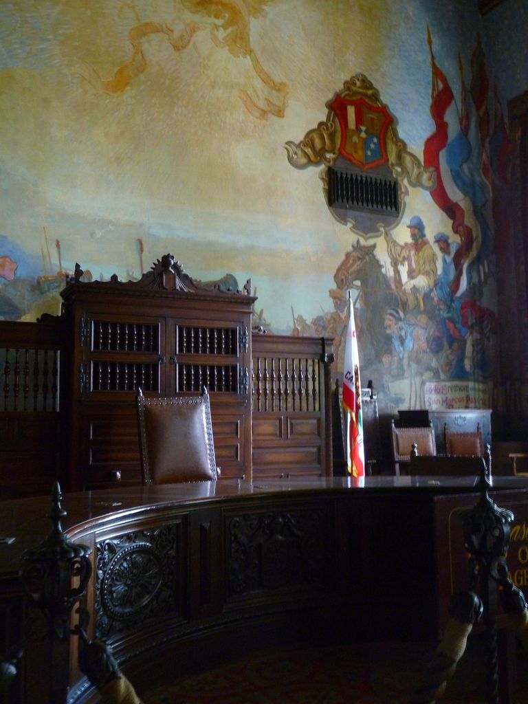 Dark carved wooden desks and chairs stand below painted figures, a mounted rider and a coat of arms.