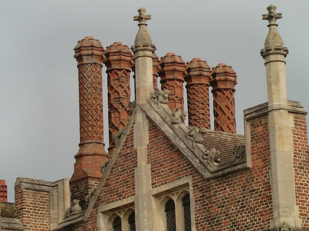 A row of tall chimney shafts carries different geometric patterns above a brick gable and stone finials.