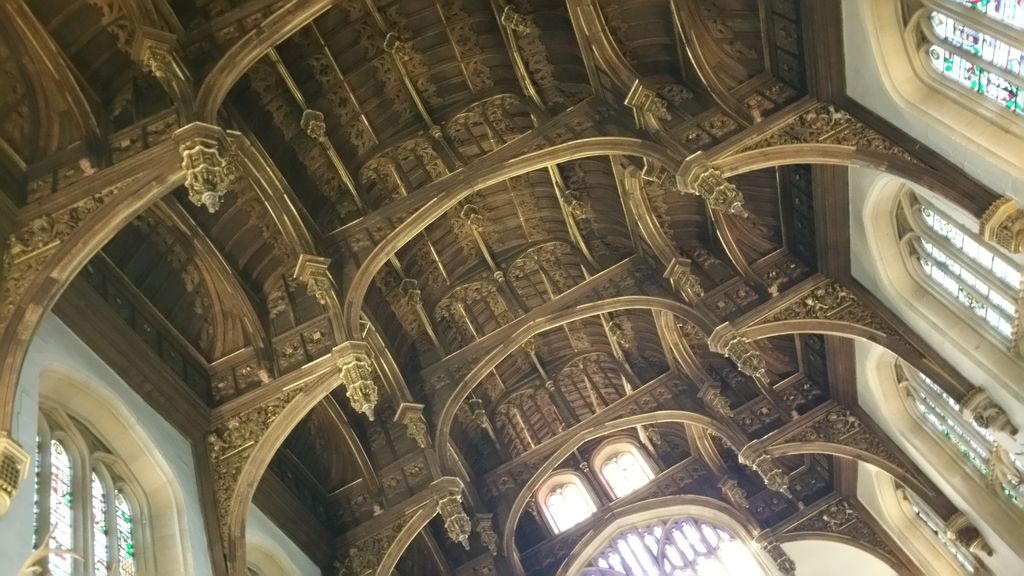 Carved hammerbeams and arched timber braces span a high hall beside bright stained-glass windows.