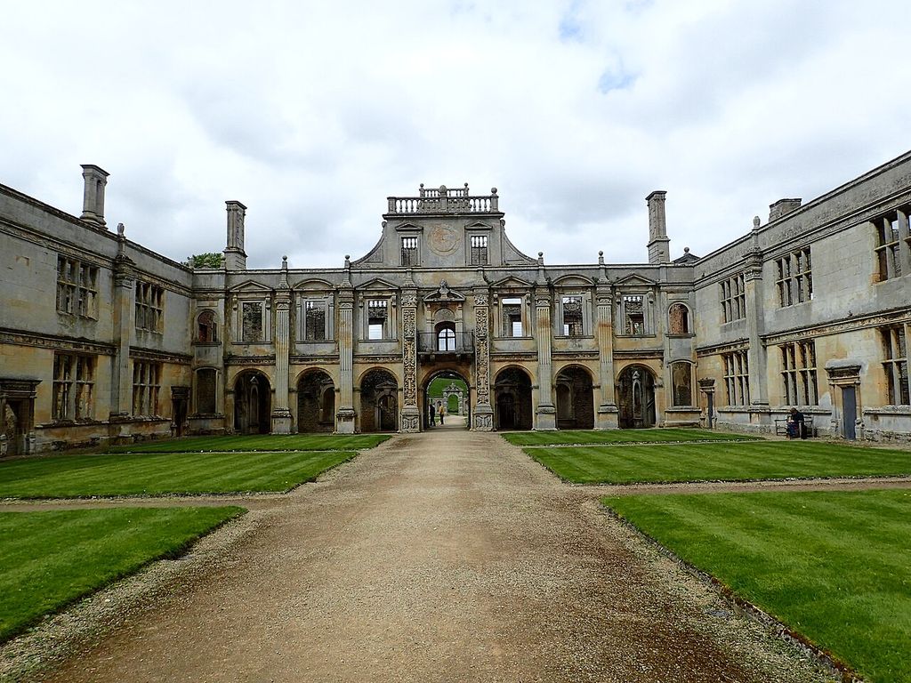 Ornamented pilasters, round arches and rows of mullioned windows line a partially ruined stone courtyard.