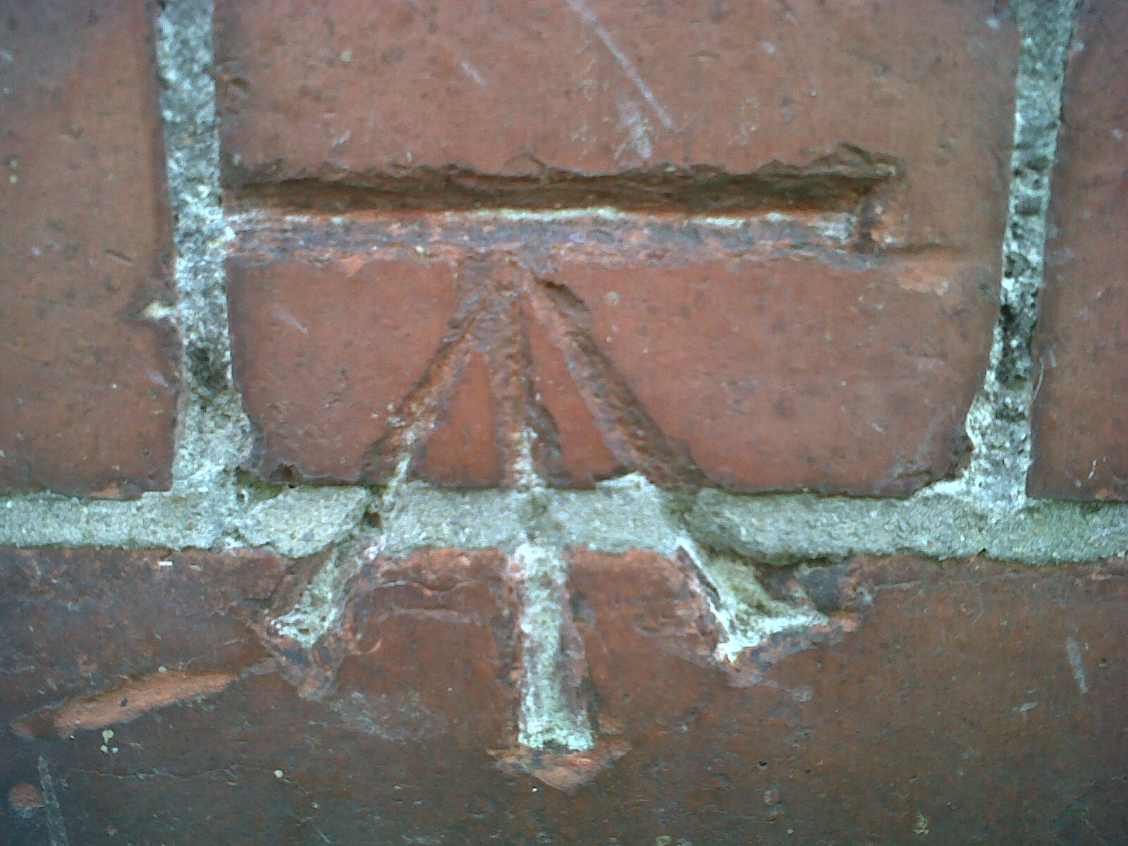 Close view of a horizontal cut and broad arrow-shaped Ordnance Survey benchmark incised across red bricks.