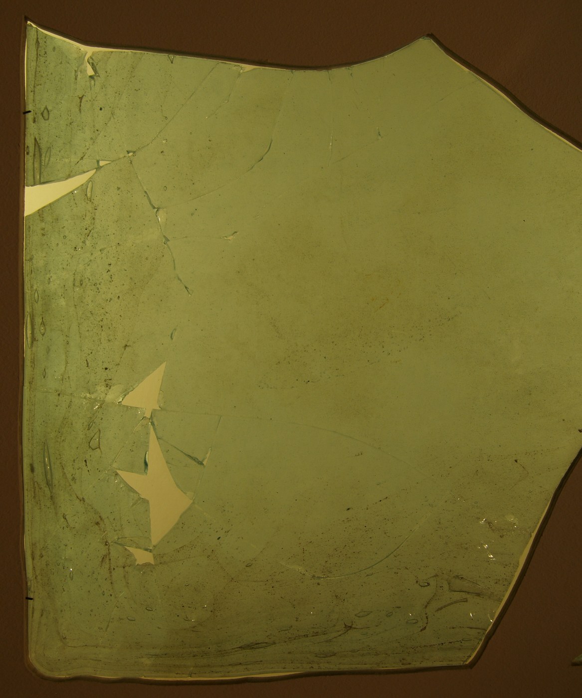 Surviving Roman window glass with an uneven surface and damaged edges.