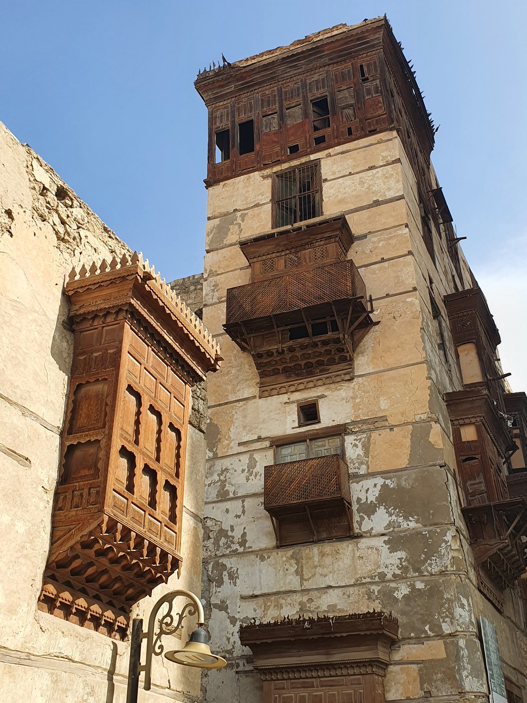 Street in historic Jeddah lined by projecting timber roshan with shutters, lattice panels and deep hoods.