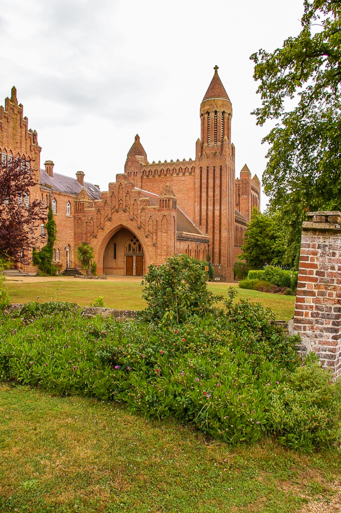 Quarr Abbey across a garden, showing red-brick church, entrance arch, stepped masses and tower.