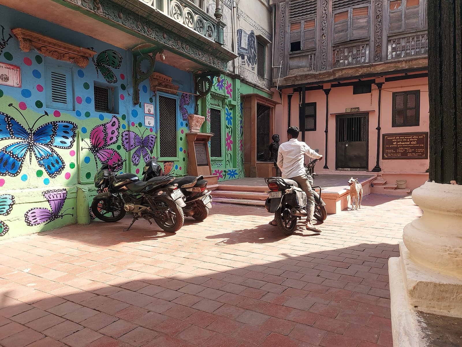 Desai ni Pol Ahmedabad house façades bordering a small open street space with motorcycles, pedestrian and dog.