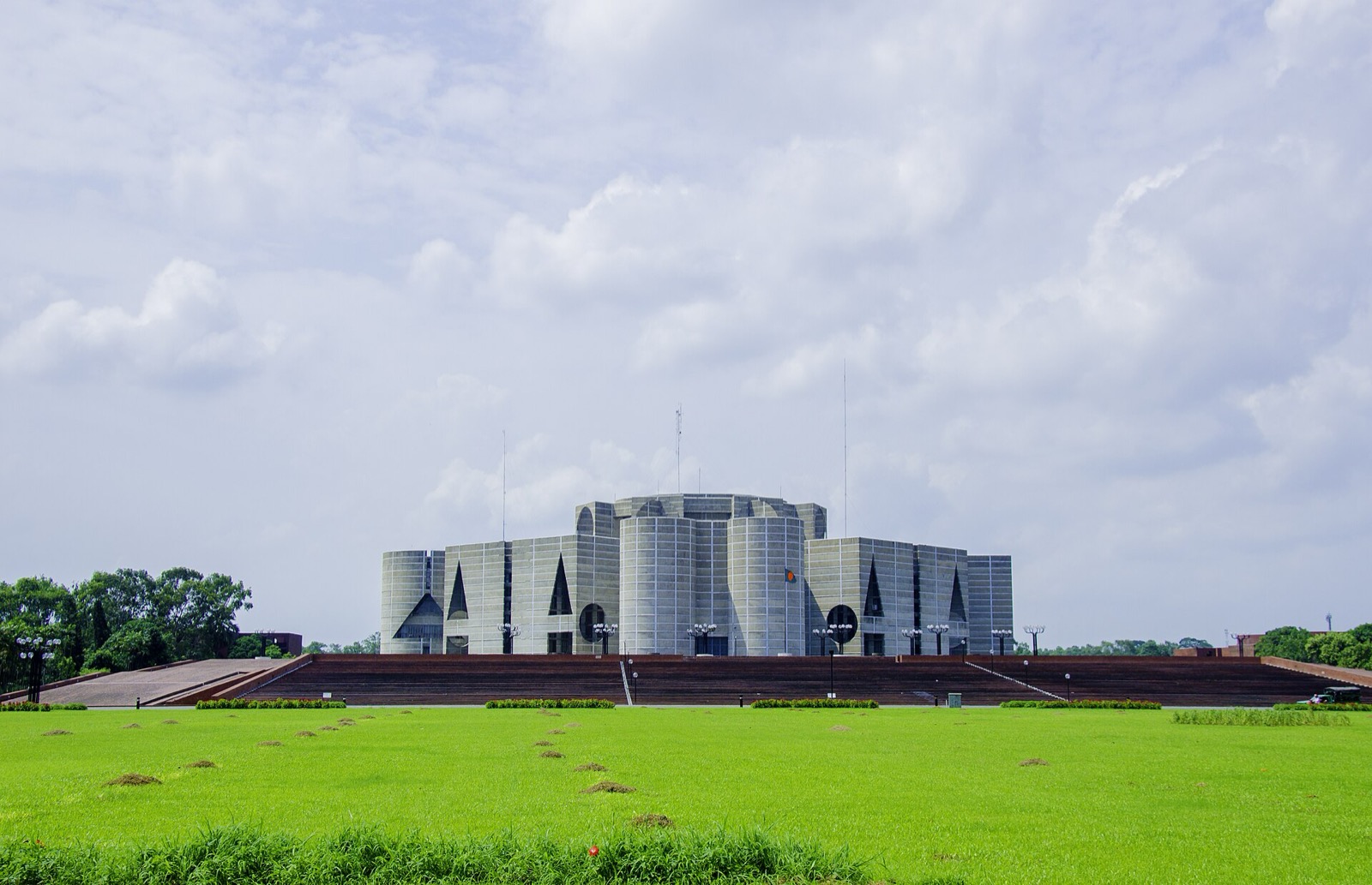 Distant frontal view of Bangladesh National Assembly Building across lawn with circular and triangular exterior openings.