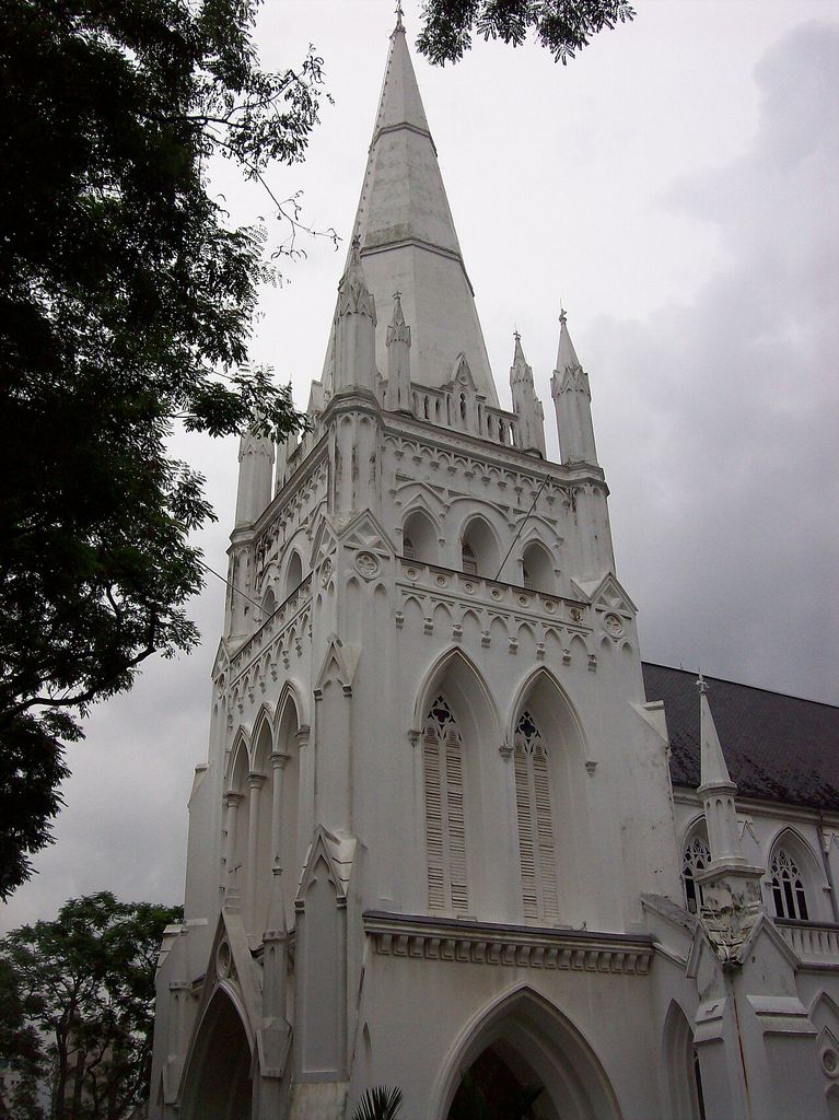 A pale Gothic tower carries pointed openings, pinnacles and a tall spire above an entrance arch.