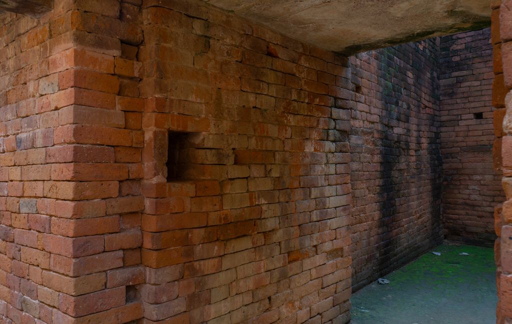 Thick red-brick walls, door openings and a narrow corridor define excavated monastic rooms with later protective work.