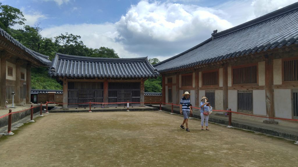 Three low timber storehouse ranges with tiled roofs enclose a quiet earthen court bordered by visitor ropes.