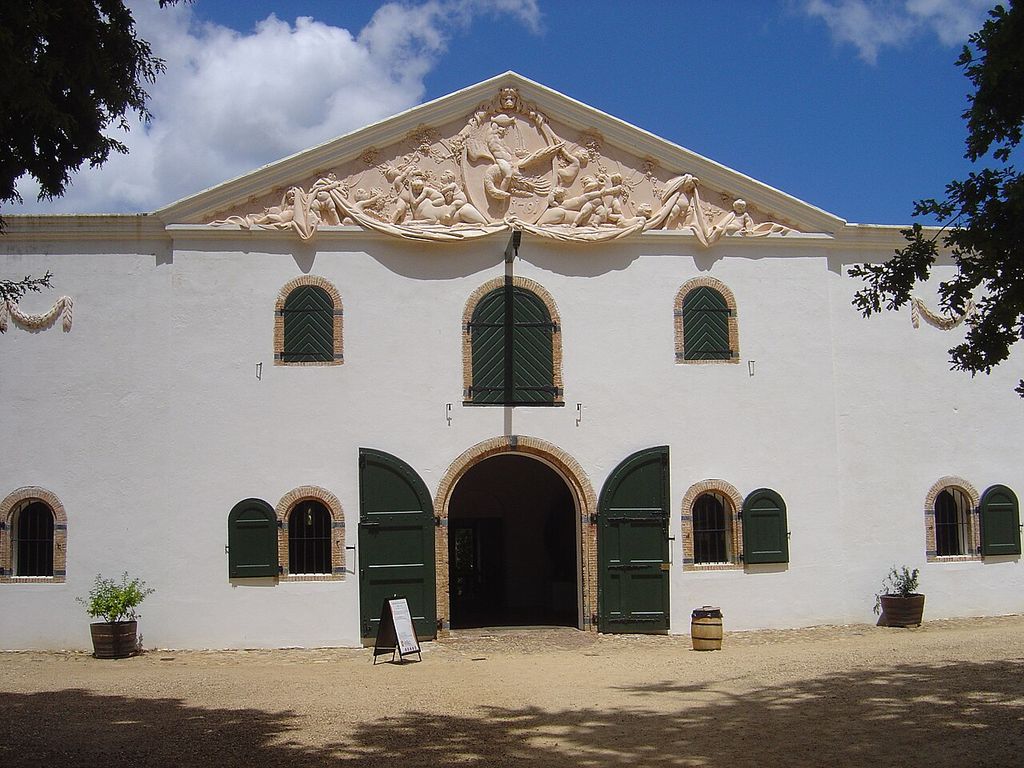 A sculpted triangular pediment crowns a rendered cellar front with arched doors and green shutters.