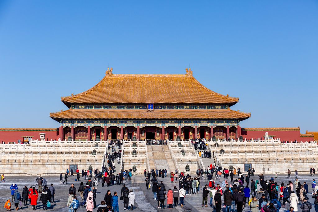A large yellow-roofed timber hall stands above white marble terraces and a broad courtyard crowded with visitors.