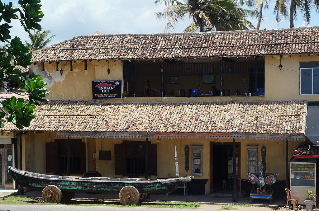 Broad tiled eaves shelter a two-storey frontage with timber posts, an open upper gallery and a restaurant below.