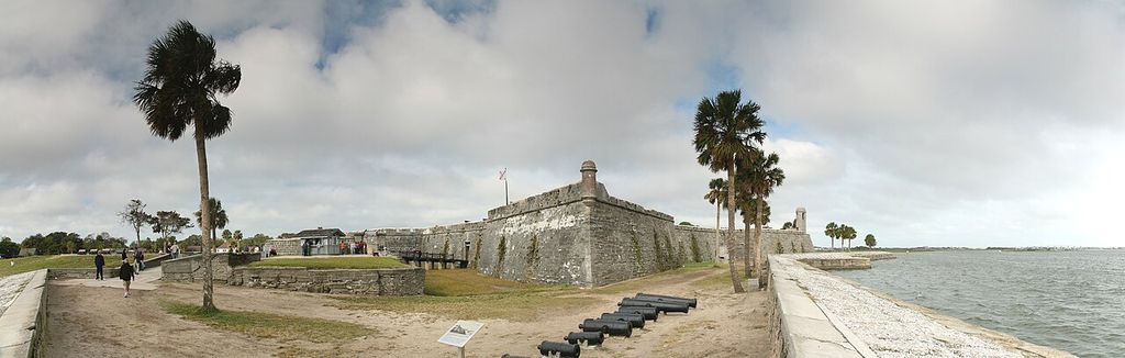 A projecting stone bastion and low defensive walls stand beside the water, with cannon displayed along the approach.