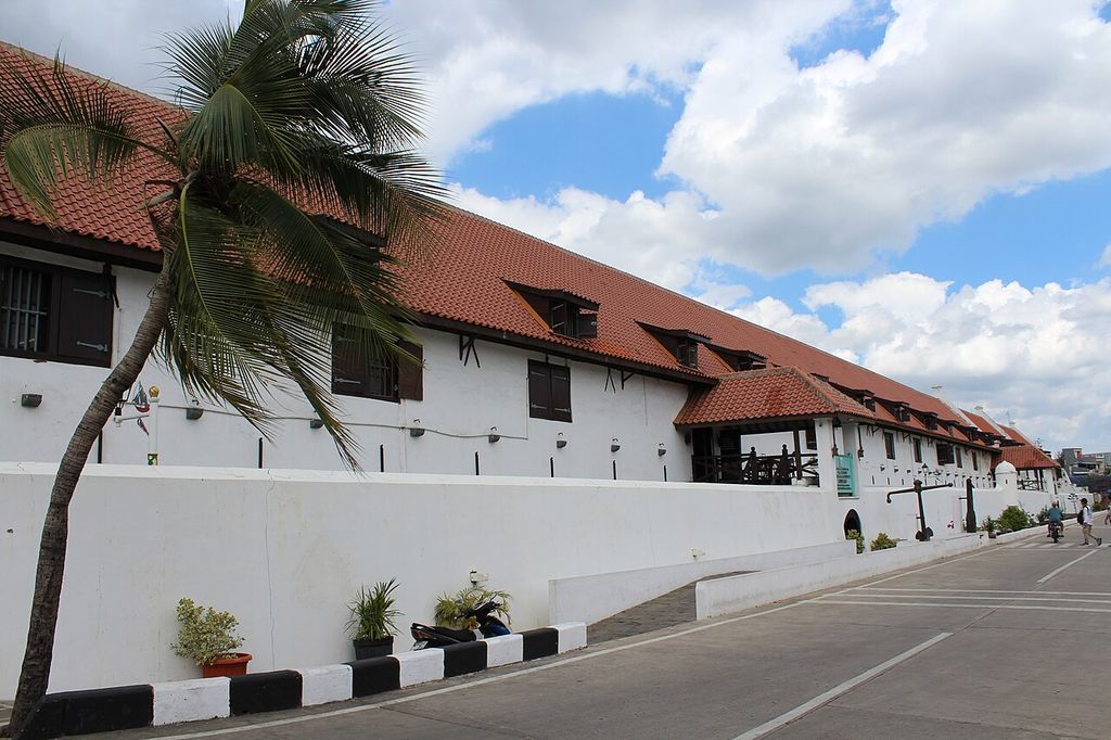 A long white-walled range with a tiled roof, dormers and shutters recedes along a street behind a low wall.