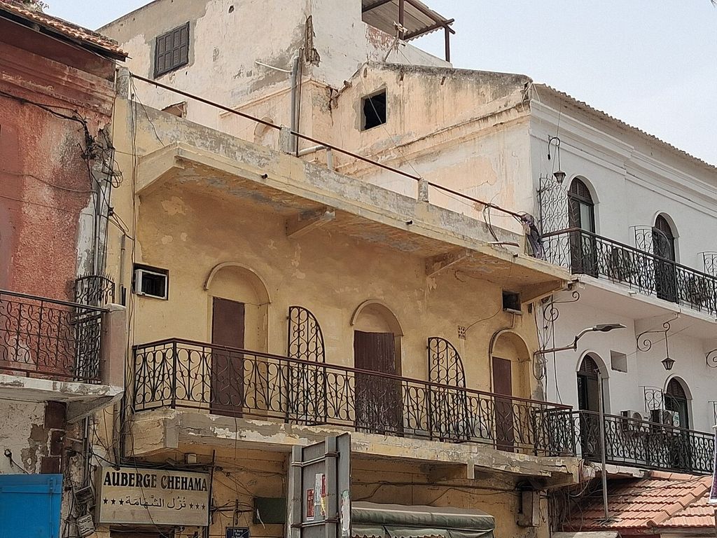 Arched openings, shutters and varied metal balcony rails line neighbouring upper floors with patched plaster and later service wires.