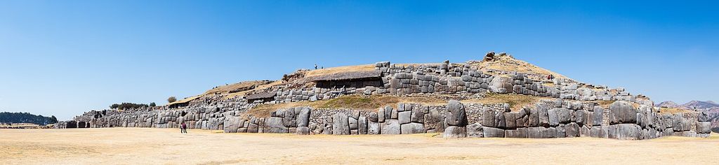 An extremely wide view shows long stepped stone walls built from huge irregular fitted blocks and smaller upper courses across open highland ground.