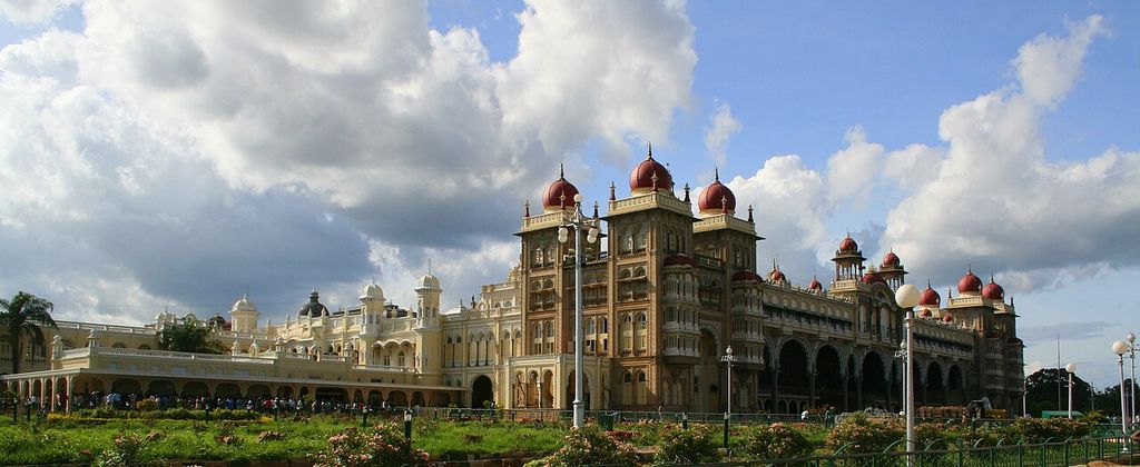 A broad palace front with arcades, towers and domes stretches behind lawns and paths.