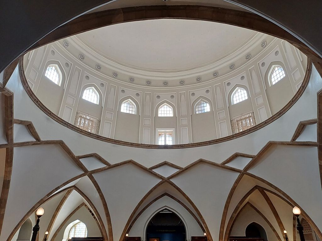 A tall domed museum space has patterned openings, intersecting arches and light entering through high windows.