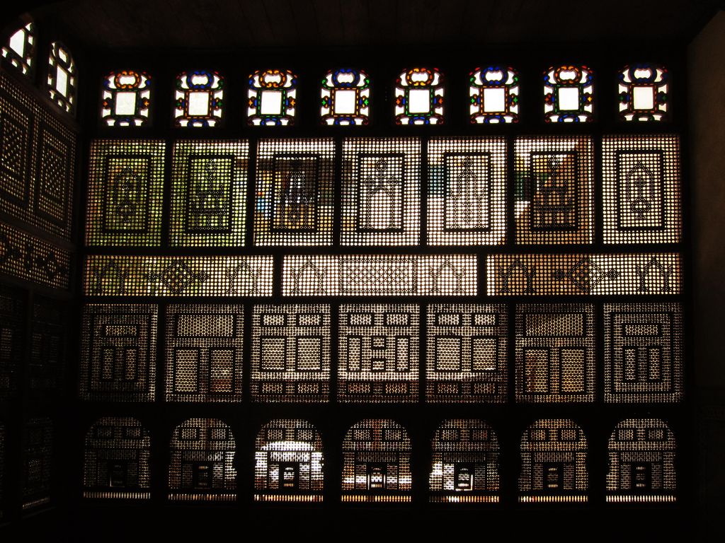 Dark timber lattice screens glow with many small geometric openings and a narrow row of coloured glass above.