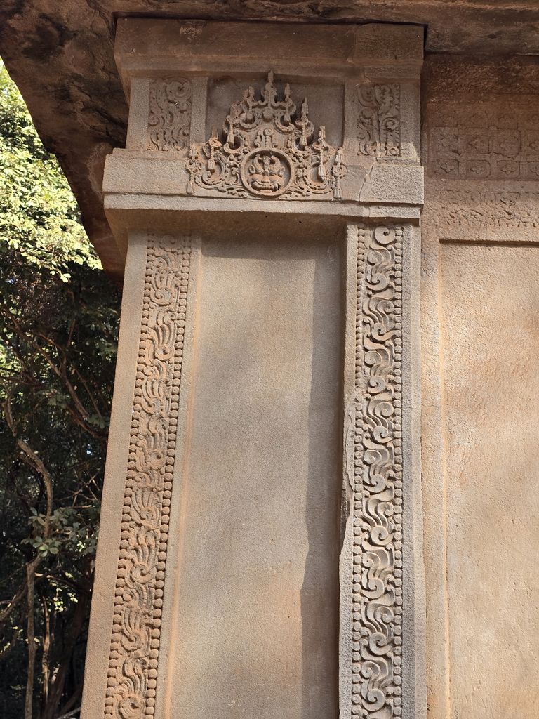 A pale sandstone doorway with carved vertical bands and lintel ornament fills a tight view beneath a roof slab.