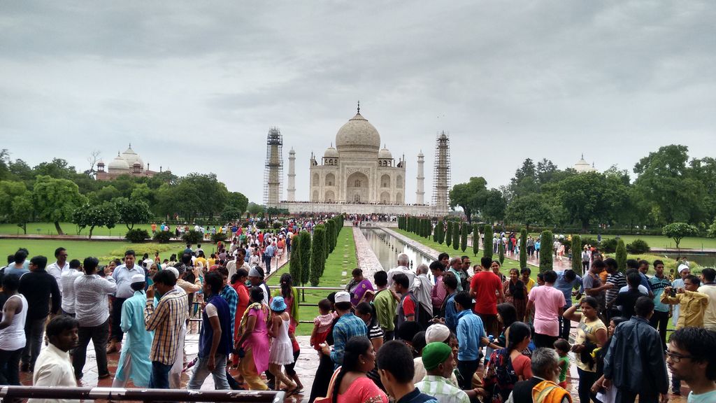 A white domed mausoleum and four minarets stand beyond a long garden path packed with visitors and lined by clipped trees.