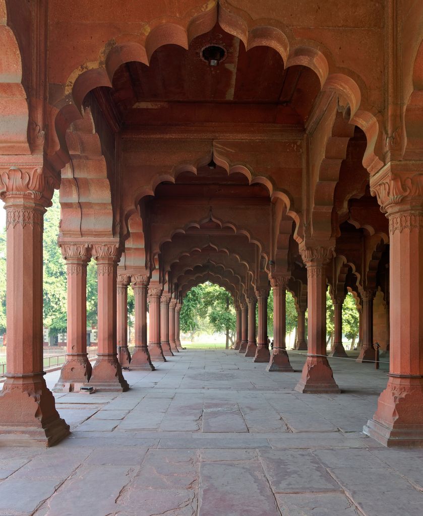 A long red-stone corridor recedes through rows of scalloped arches and columns toward bright trees.