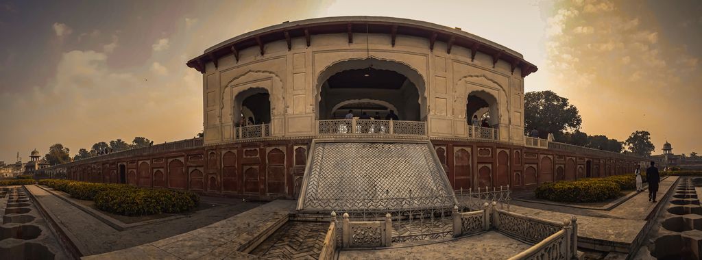 A very wide view shows an octagonal pavilion beyond a large dry stepped basin, low red walls, gardens and trees at sunset.