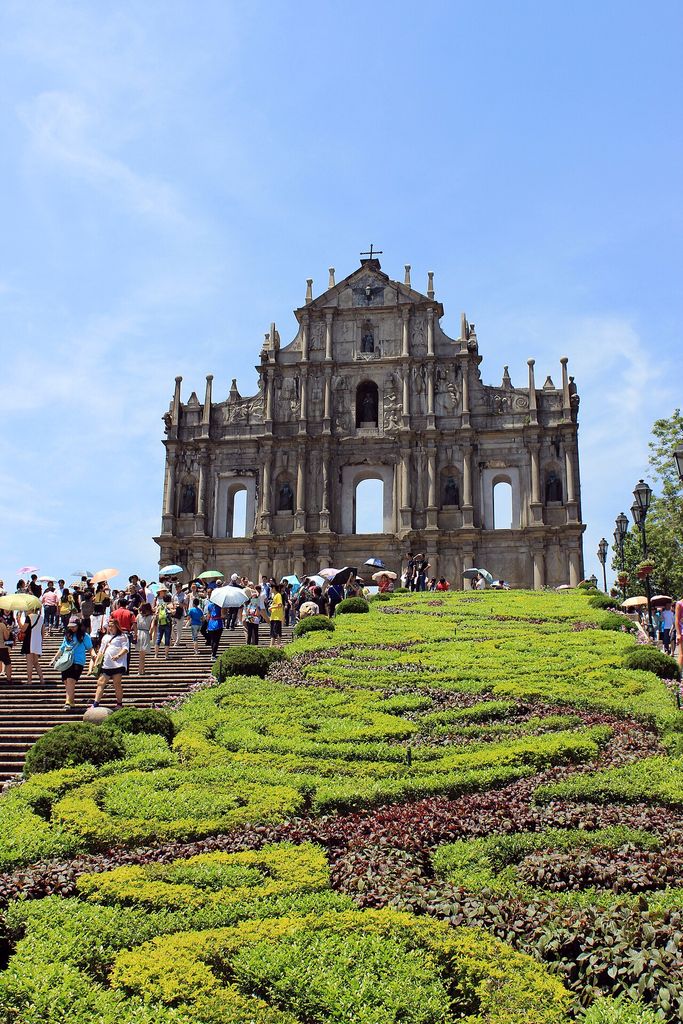 A tall carved stone façade stands open to the sky above broad steps and a landscaped slope.