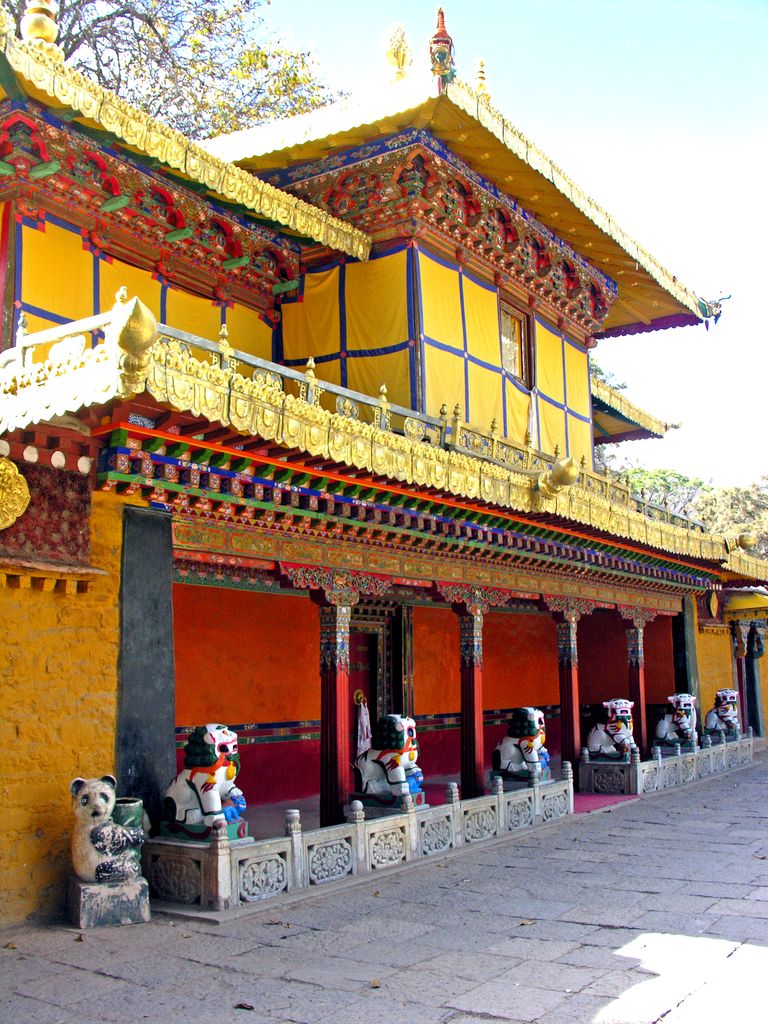 A yellow palace pavilion with painted timber brackets, dark windows and gilded roof edges stands behind a low white balustrade.