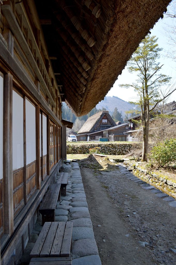Thick thatch projects over timber roof members and a wooden frontage beside a narrow stone-edged path.