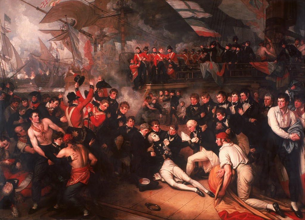 Nelson reclines among officers on a crowded ship’s deck, with wounded sailors, raised hands, sails, rigging and smoke extending around and above him.