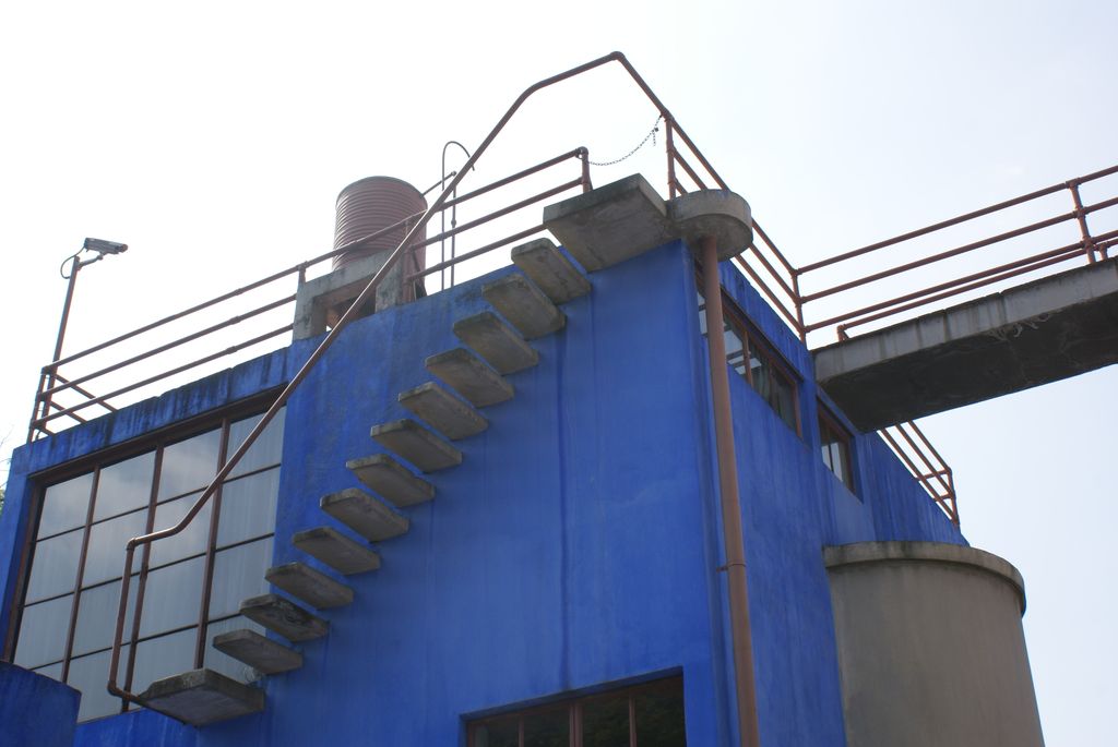 Blue and white studio building with an exterior cantilevered stair and rooftop bridge.