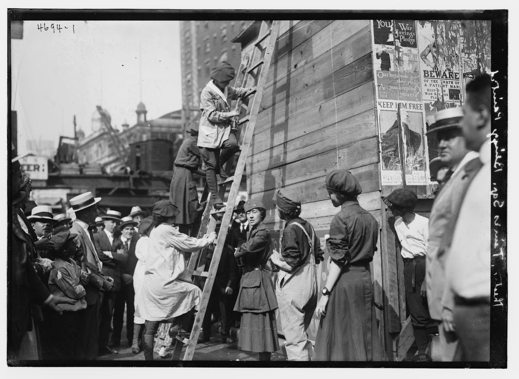Workers painting large theatre signs high above Times Square in an early twentieth-century photograph.