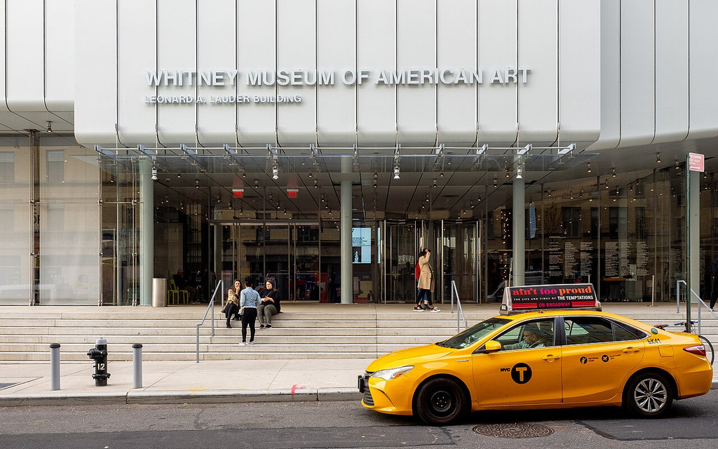 Entrance to the Whitney Museum with a yellow taxi in front.