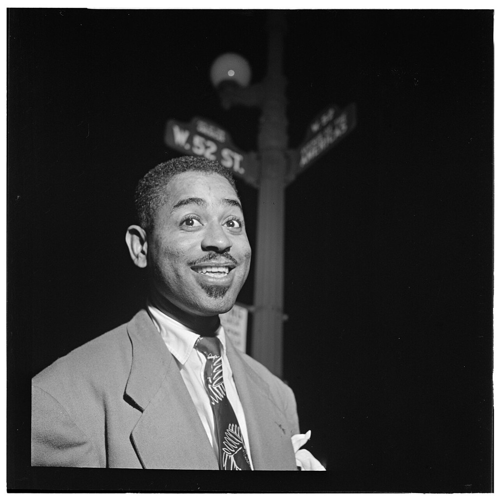Dizzy Gillespie smiling beneath New York street signs.