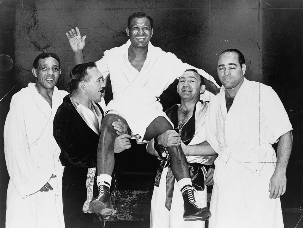 Sugar Ray Robinson in a white robe, waving while other boxers lift him.