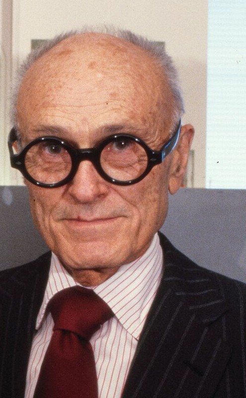 A portrait detail of Philip Johnson wearing round black glasses and a red tie.