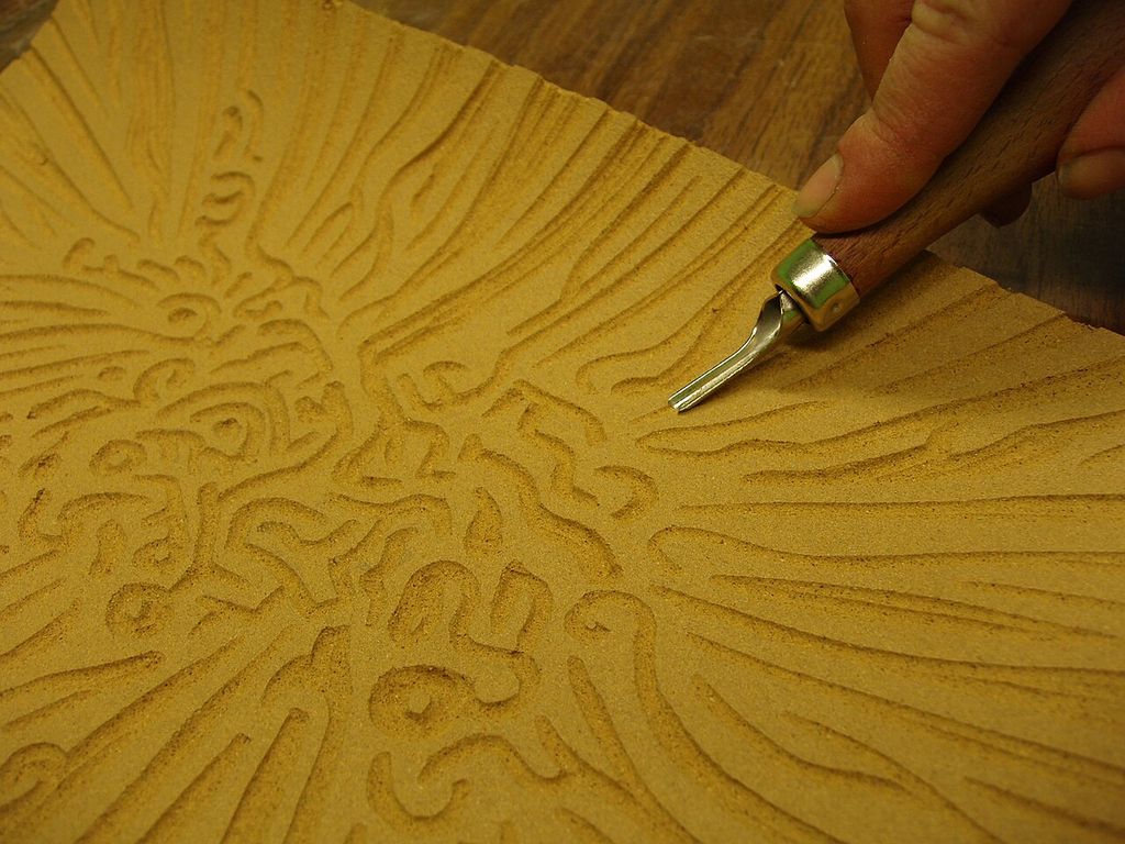 Carving a linocut block: the removed areas will not carry ink in the final impression.