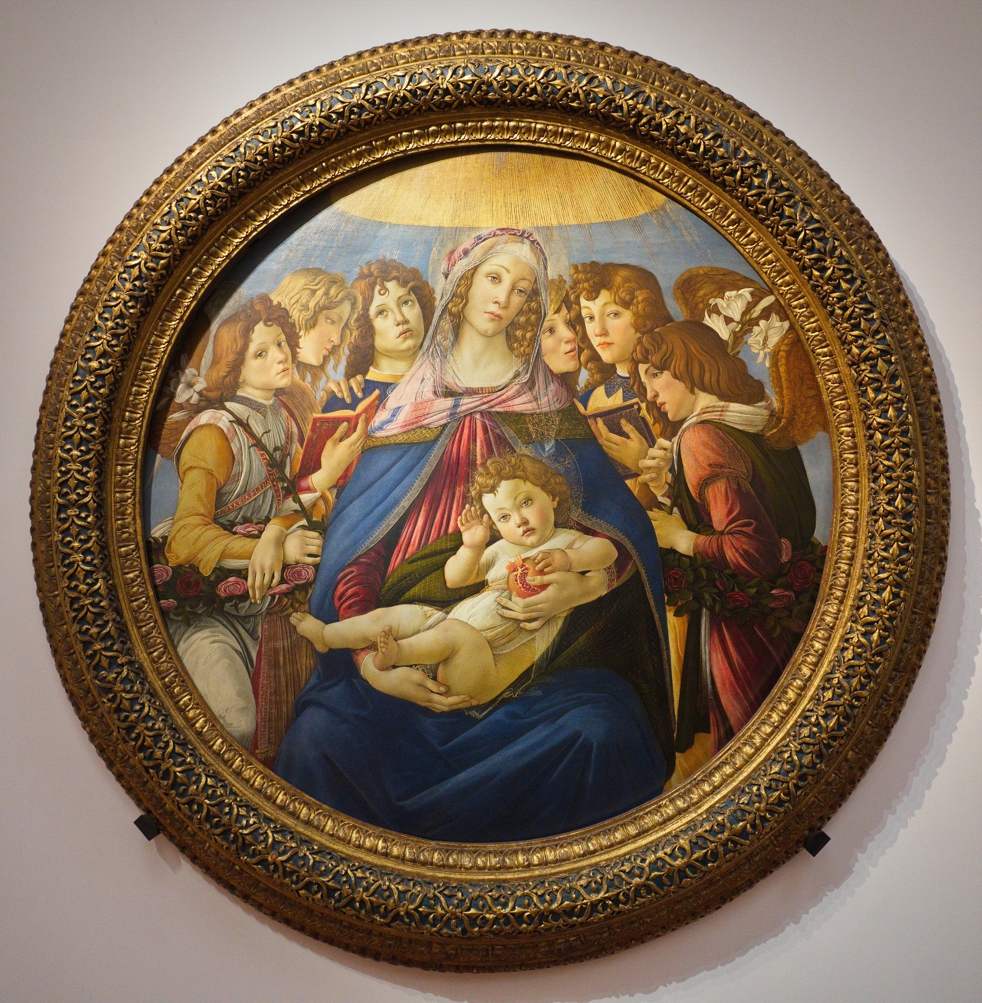 Virgin Mary seated with the Christ Child holding a pomegranate, surrounded by six angels in Botticelli's circular painting.