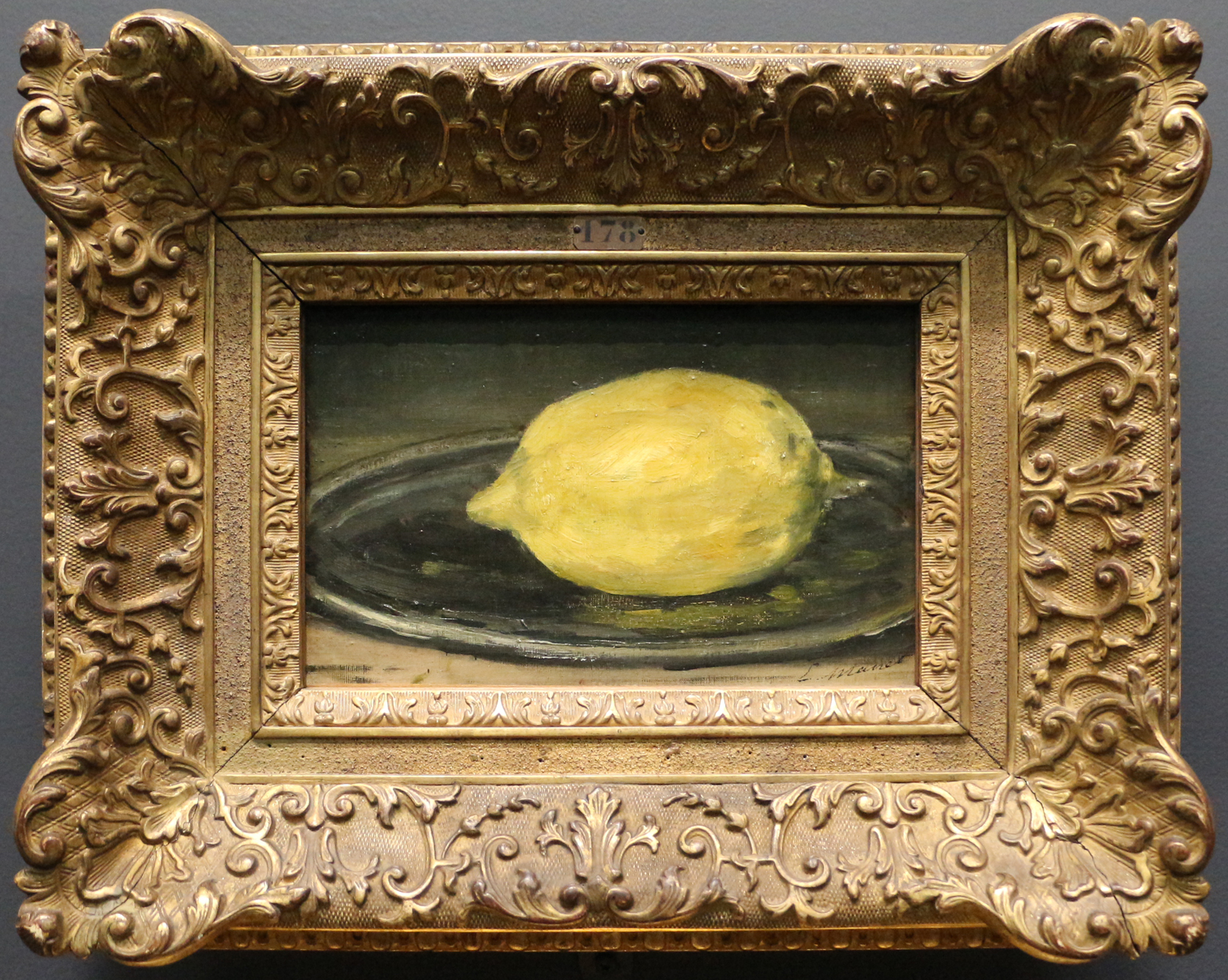A single yellow lemon rests on a dark plate within the ornate frame of Manet's small still life.