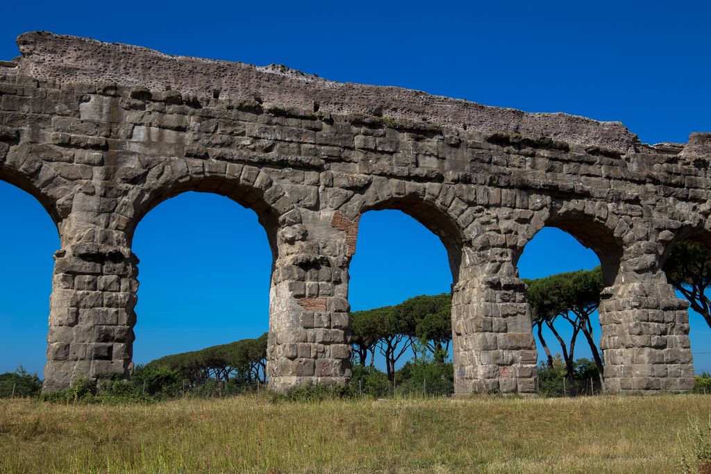Tall stone and brick aqueduct arches seen close up against a blue sky in Rome