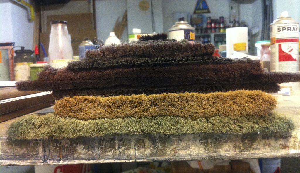 Several large broad brushes stacked in a studio, showing wide rectangular heads and long handles.
