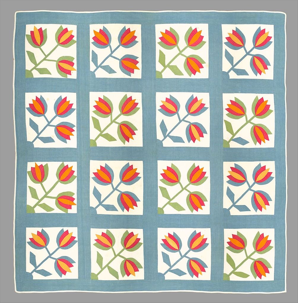 Sixteen white quilt blocks repeat red, orange and yellow tulips with alternating green and blue leaves inside a pale blue surround.