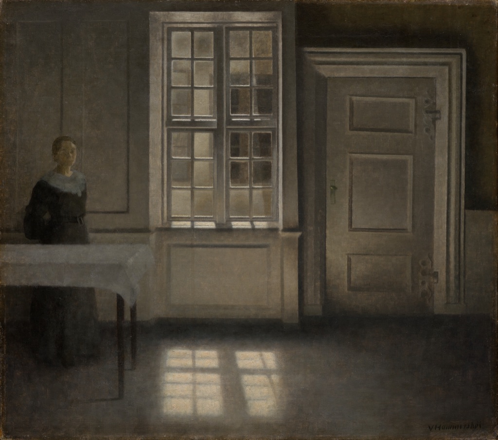 A dim brown and gray interior contains a woman, window, closed door and pale rectangles of reflected sunlight on the floor.