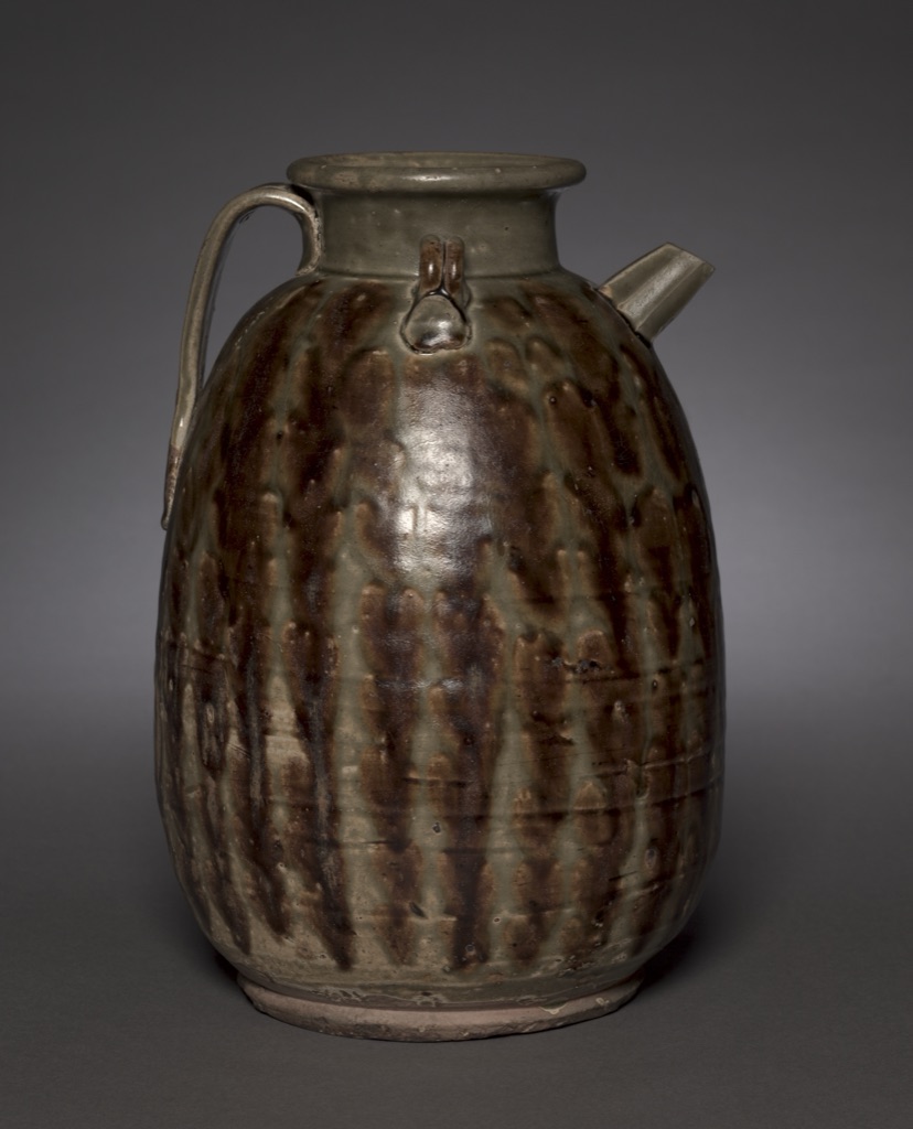 A rounded Tang stoneware ewer has an olive-green glaze crossed by irregular glossy iron-brown vertical splashes, with handle and short spout.