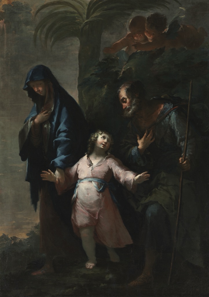 A pale pink-clad child stands between blue-draped Mary and dark-robed Joseph while deep foliage and shadow surround the illuminated figures.