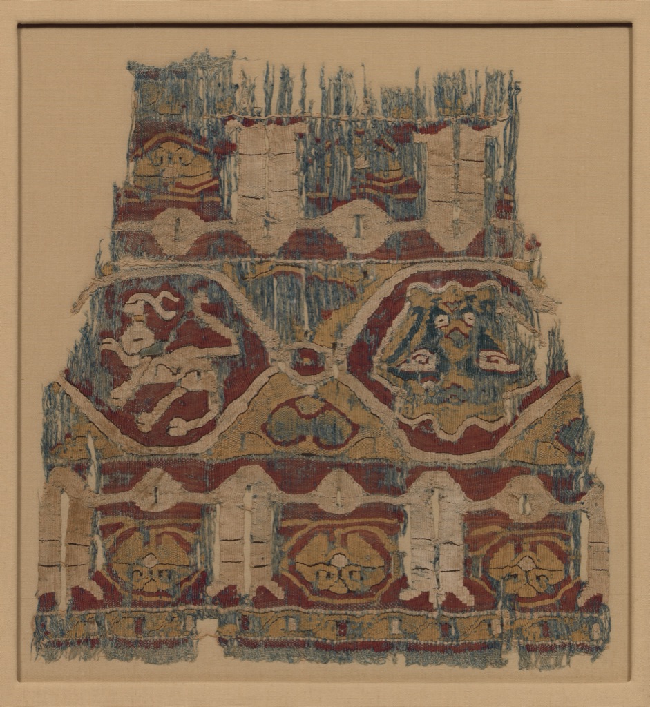 A worn linen-and-silk fragment repeats muted red, blue and yellow bands, medallions, animals and inscription-like forms.