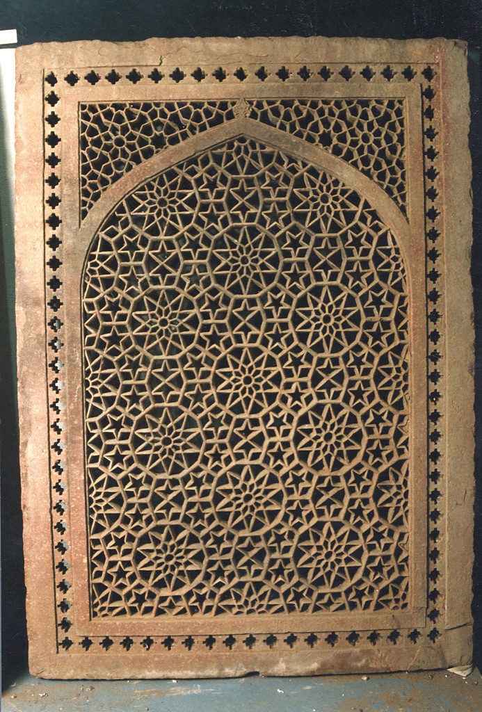 The complete rectangular red sandstone screen contains an arched field of dense geometric openings within a solid frame.