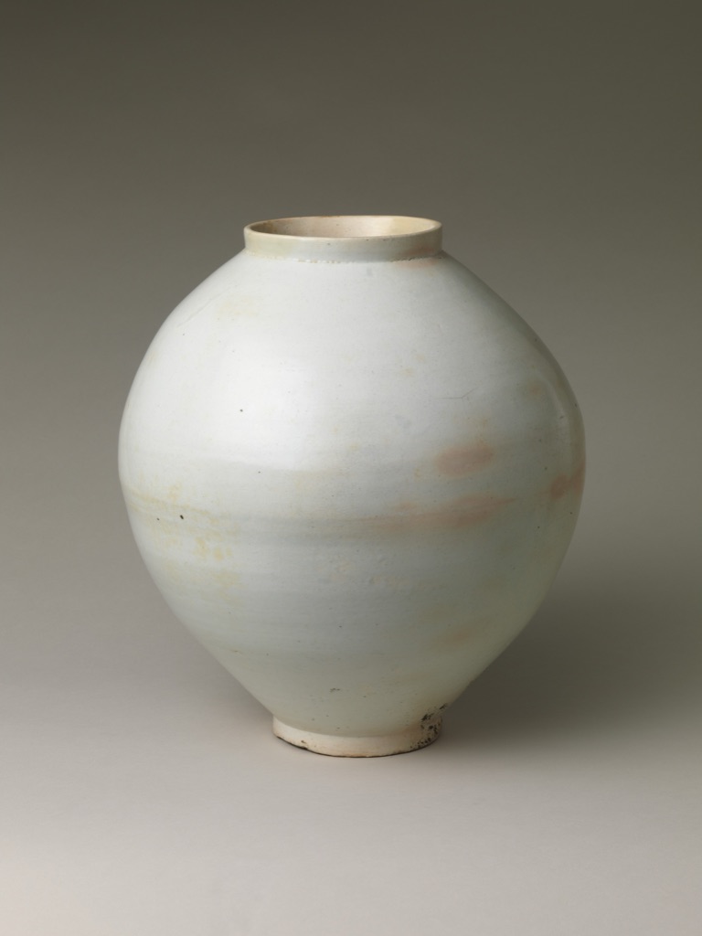 A large Korean white porcelain moon jar appears against a grey background, with gentle light and shadow across its rounded body.