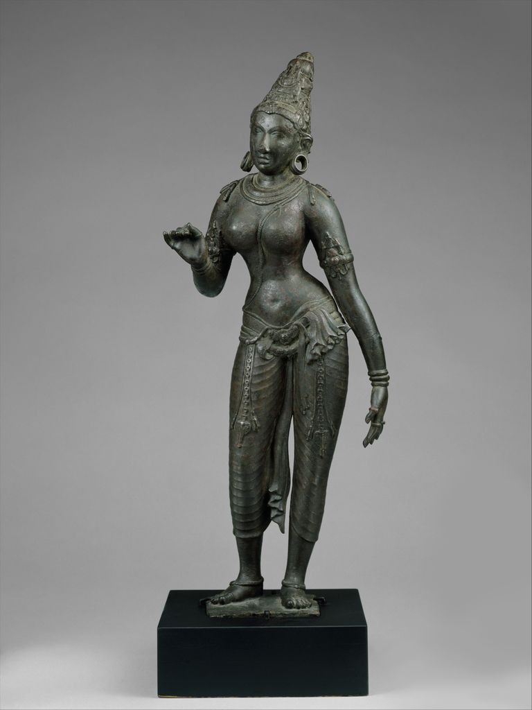 A Chola copper-alloy image of Parvati stands upright with a tall headdress long arms and a narrow waist.